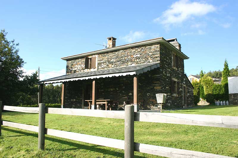 La casa completa de piedra, con su porche, pradera y cerca de madera.