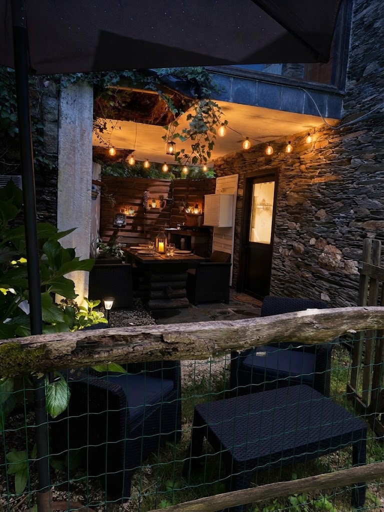El Buxo: patio con mesa, vegetación y luces al anochecer.