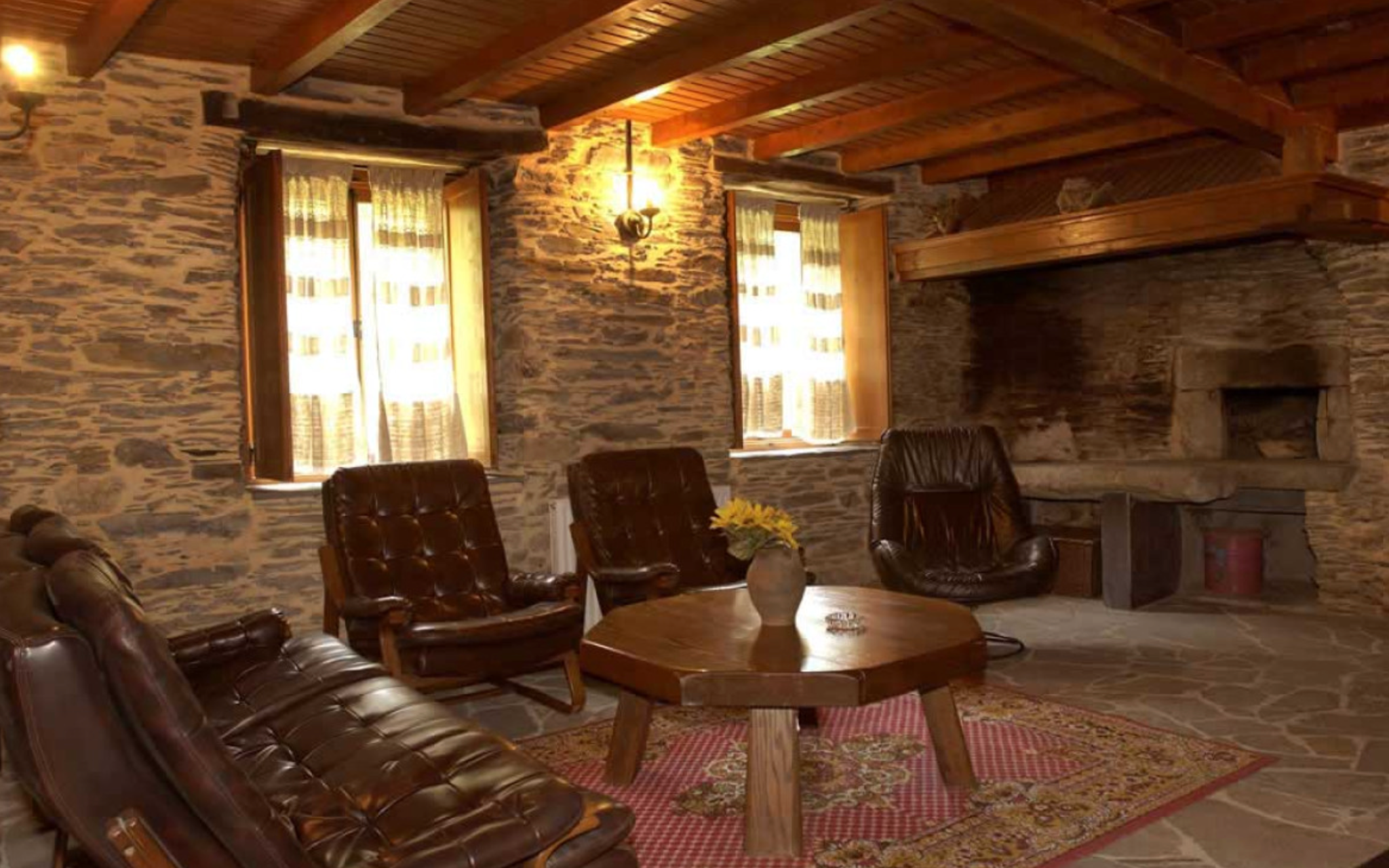 Sofá y butacas alrededor de una mesa, junto a la chimenea de piedra.